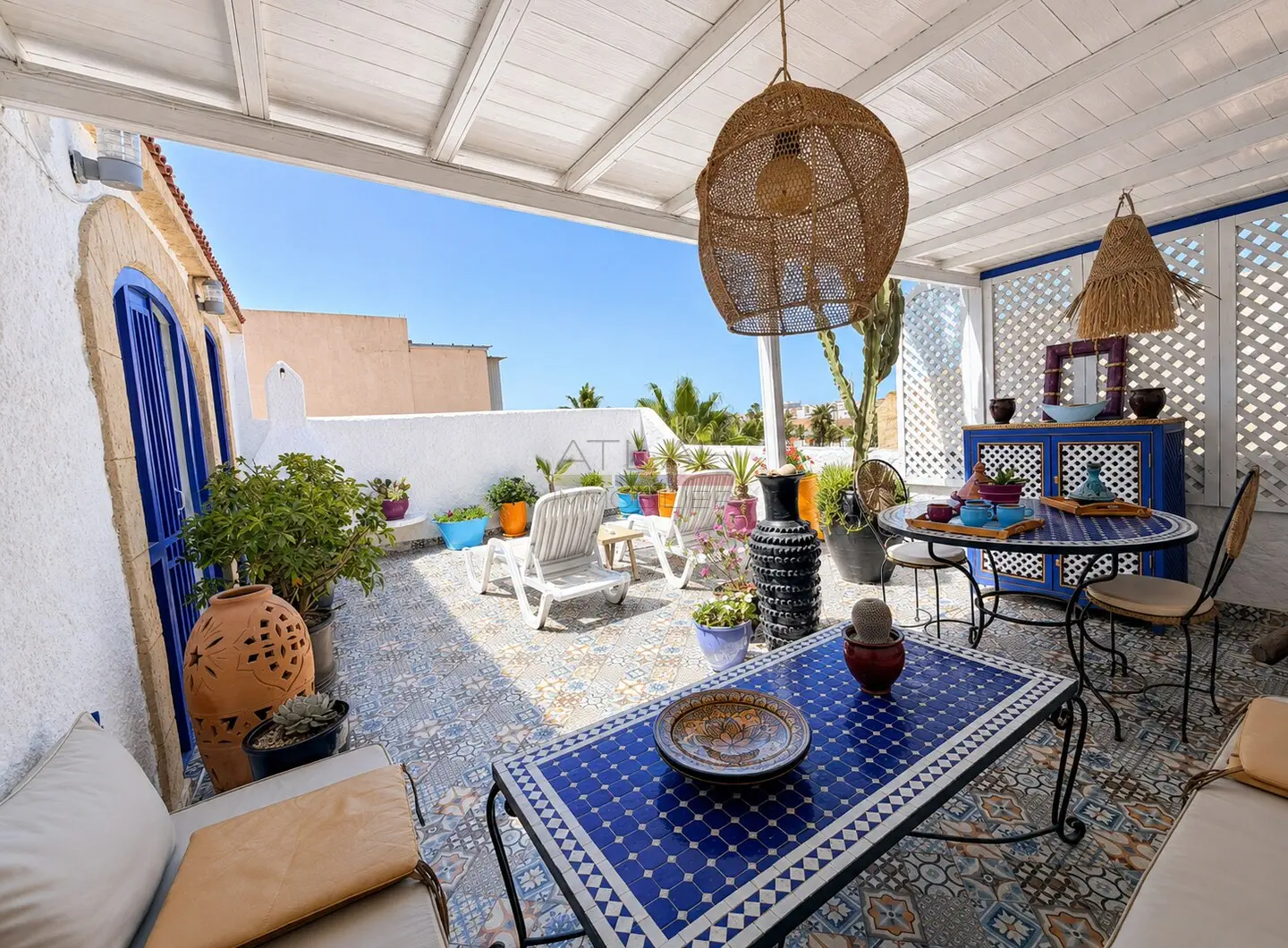 Terrasse aménagée sous pergola d’un riad à Essaouira avec portes bleues et plantes en pots