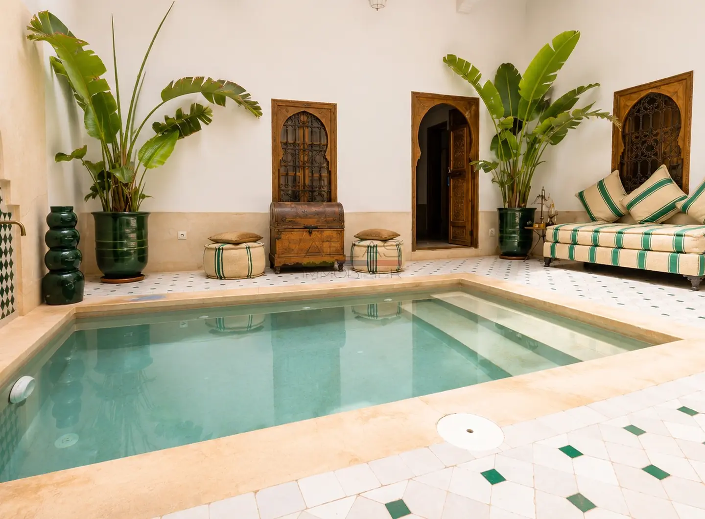 Piscine centrale et salon aménagé dans le patio d’un riad à Marrakech