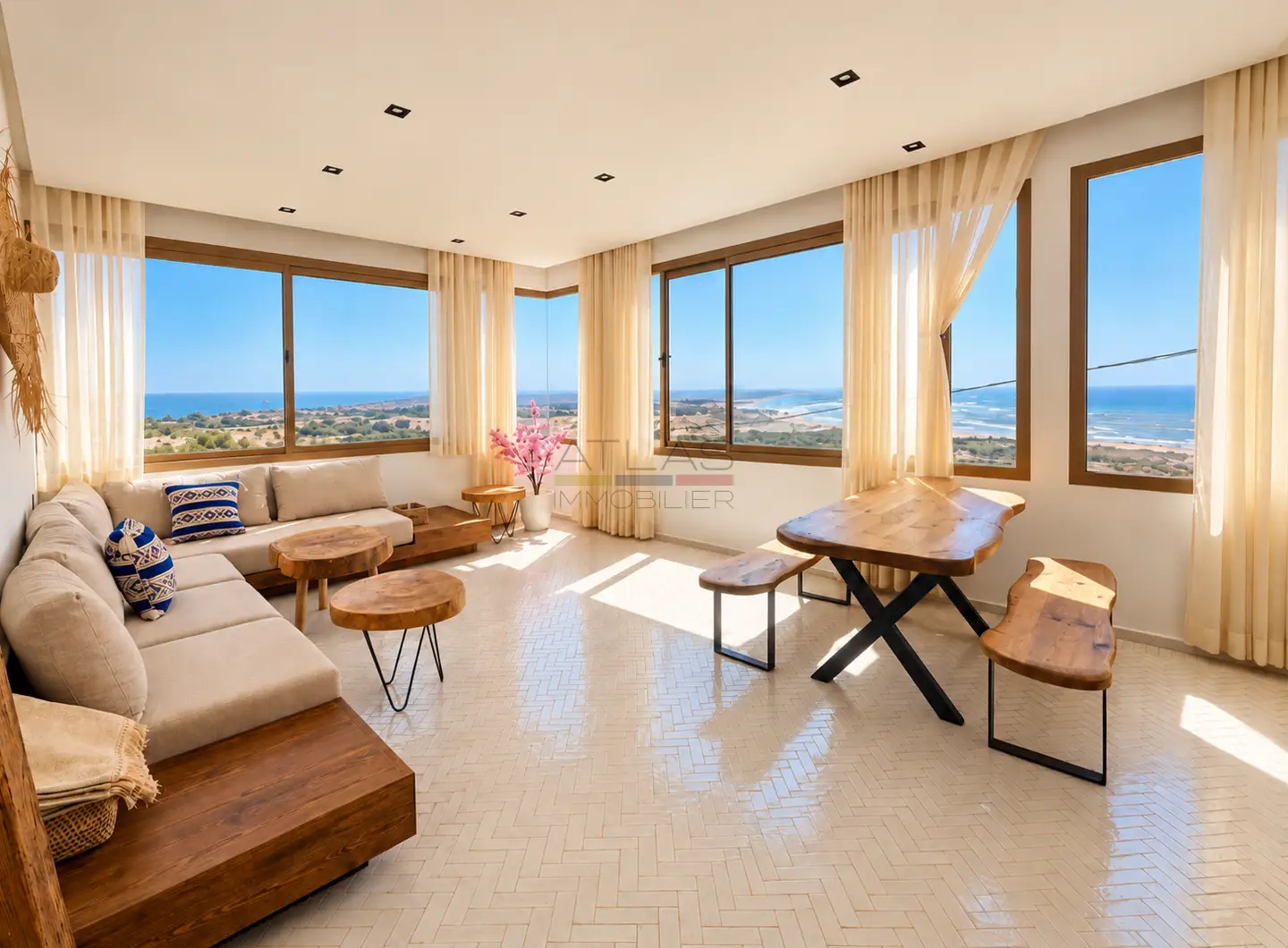 Bright living room in a villa in Ouassane, featuring large panoramic windows, comfortable sofas, a dining area and unobstructed views of the Atlantic Ocean.